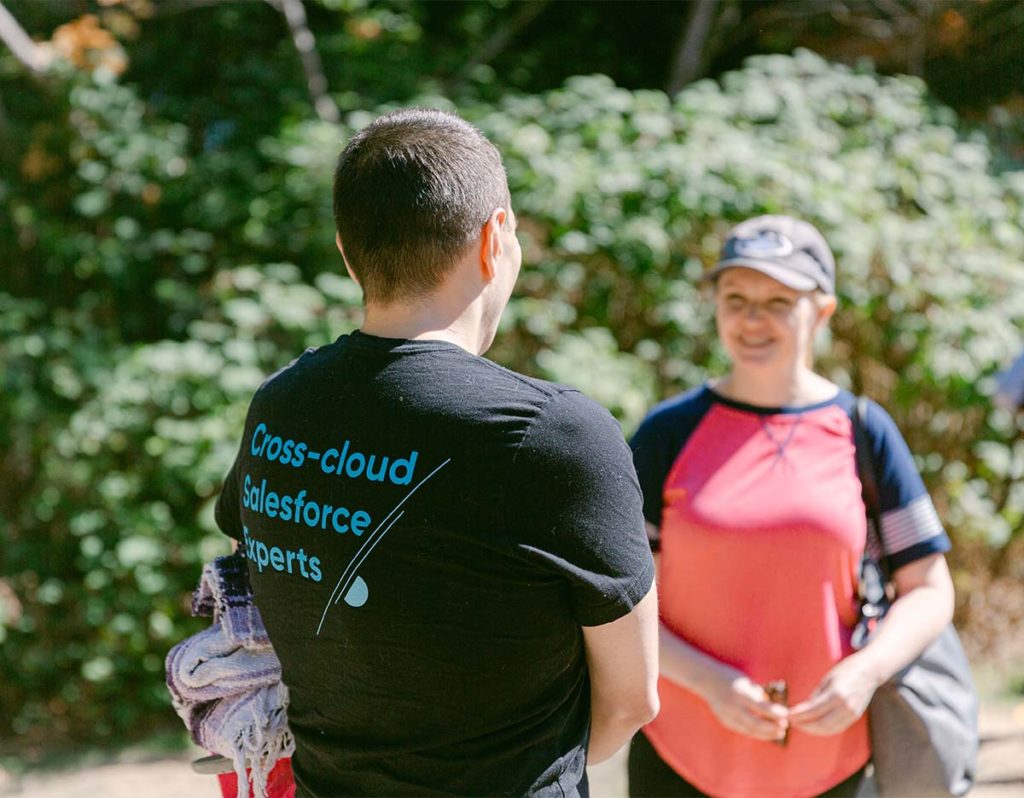 a gentleman's back is turned to the camera and on the back of his black t-shirt in blue lettering it Cross-cloud Salesforce technical  experts 